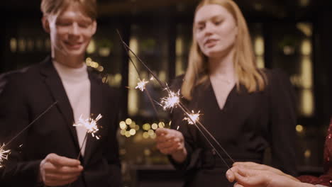 close up view of group of friends wearing stylish clothes dancing and holding sparklers at new year's eve party