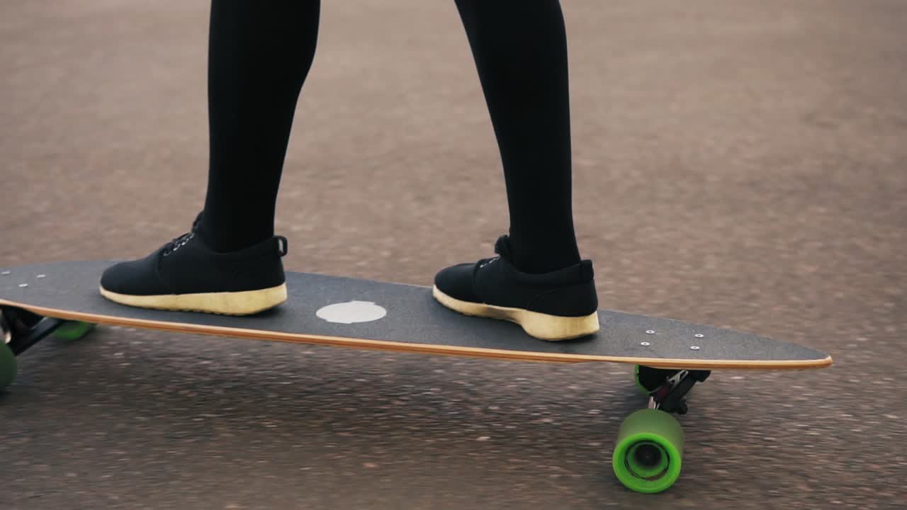 Close Up view of woman's legs in black sneakers skateboarding on the road in the city. Legs on the skateboard. Slow Motion shot