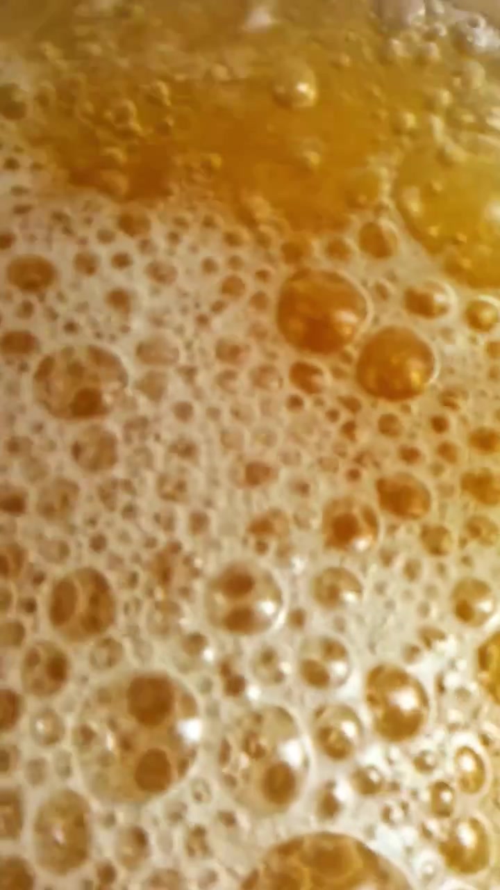 Un bicchiere si riempie di birra dorata che vortica mentre la schiuma ambrata sale e si formano bollicine dense, incarnando il semplice piacere e l'attrattiva visiva di una bevanda fredda appena versata