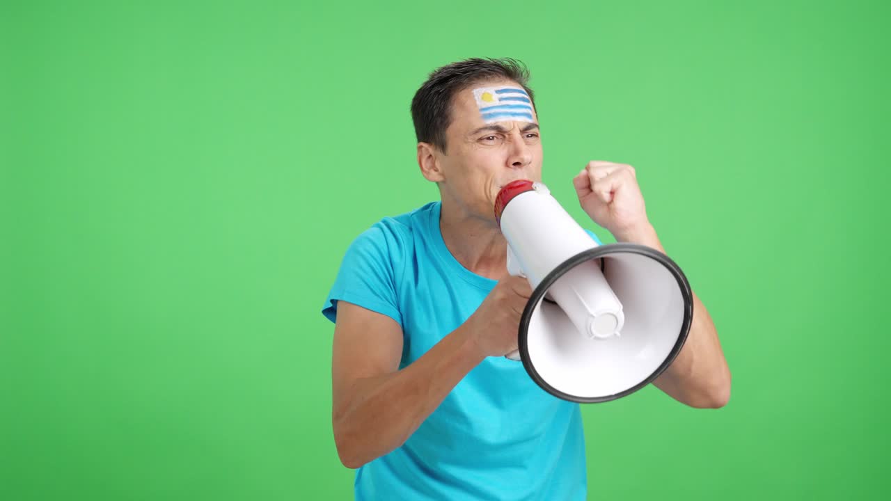 Excited man with uruguayan flag on face using a megaphone