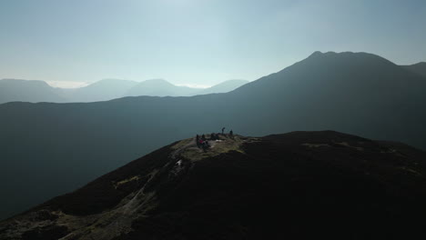 hikers on mountain summit with pull back revealing panoramic view of misty mountains in english lake district uk