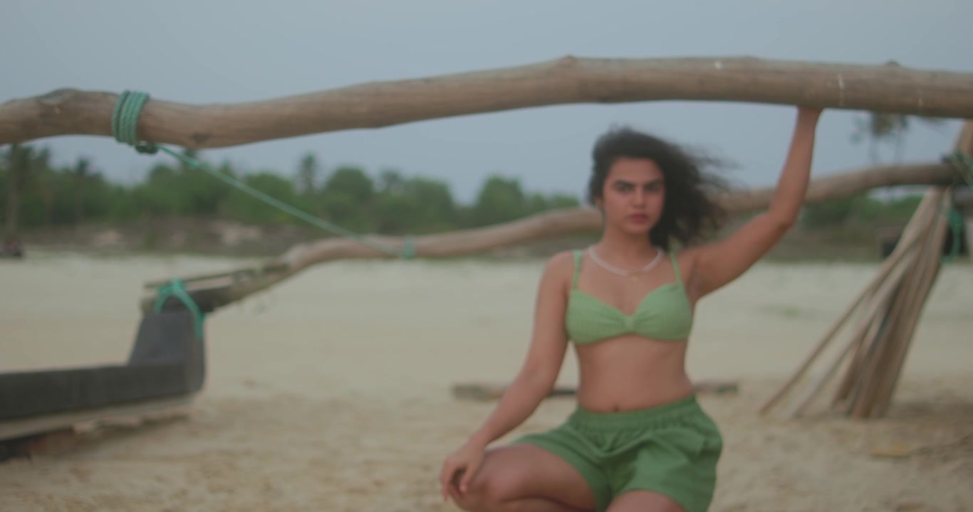 Inquadratura cinematografica sfocata di una donna inginocchiata sotto una trave di legno di una barca su una spiaggia.