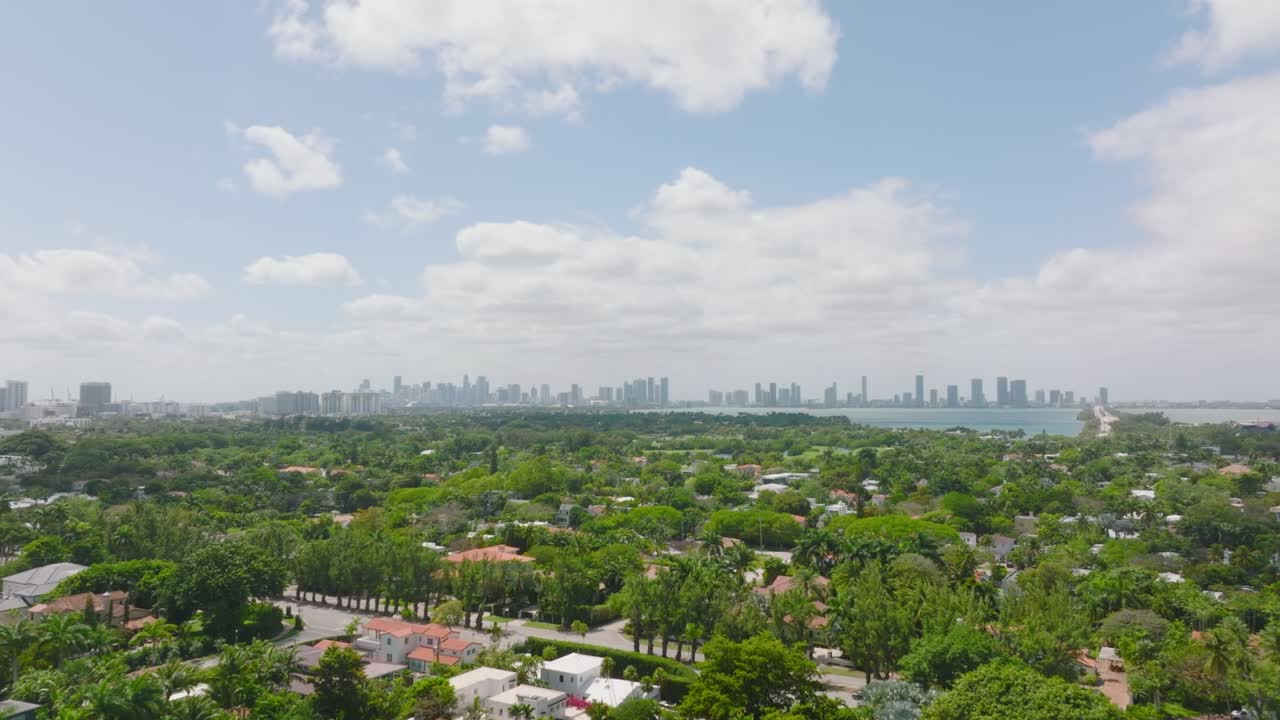 포워드는 초록색으로 둘러싸인 가족 주택과 거주지와 함께 주거 지역 위를 날아갑니다. 멀리 있는 마천루와 함께 스카이라인. 마이애미, 미국