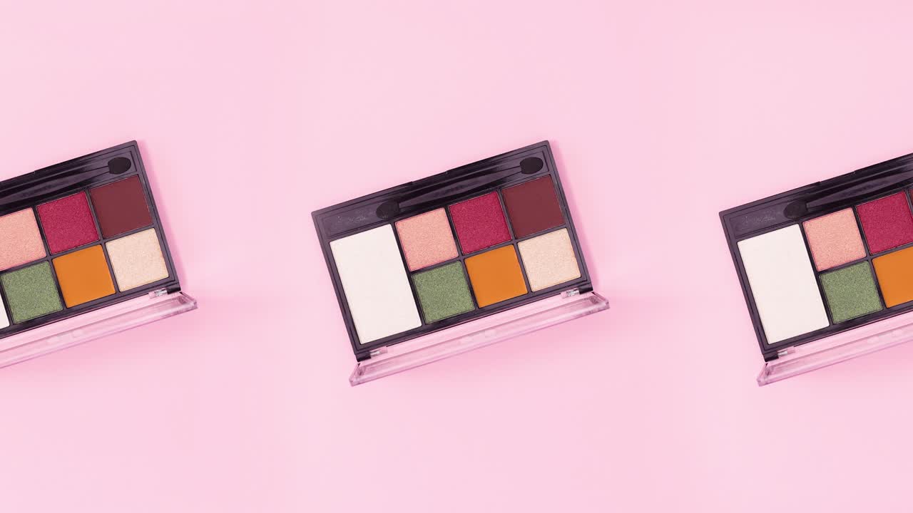 Three colorful eye shadow palettes rotating on bright pink background. Stop motion