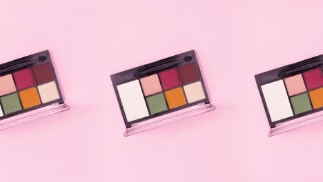 tres paletas de sombras de ojos de colores girando sobre un fondo rosado brillante. detenga el movimiento