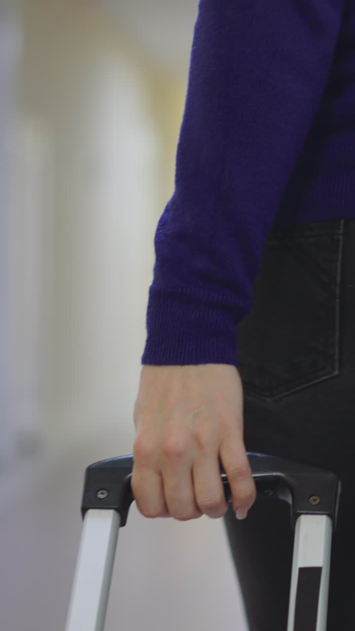 mujer camina en el largo corredor del hotel sosteniendo el mango de la maleta. viajera femenina con equipaje busca habitación después de su llegada al hotel vista trasera cercana