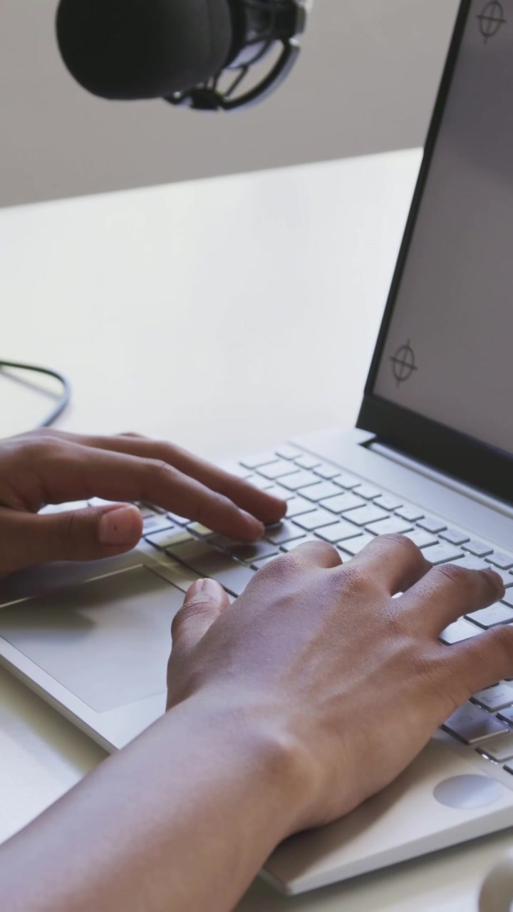 Hænder lander på hjemmerække og taster på bærbar computer, håndled skifter position, mikrofon optager.