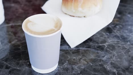 african american male barista putting cup of coffee and fresh roll on table in bakery in slow motion