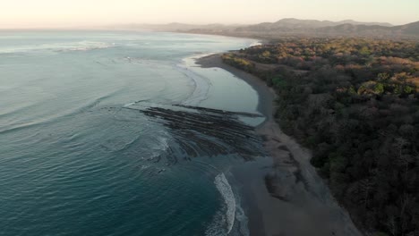 a aerial view of a beautiful sunrise over a beach in costa rica, with waves crashing on the coastline and the reef making a really beautiful shape