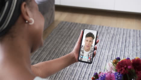 mujer afroamericana sosteniendo un teléfono inteligente con un hombre biracial en la pantalla