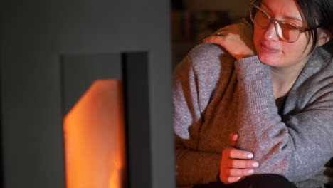 Woman-stares-contently,-enjoying-the-warm-glow-of-cosy-indoor-fireplace