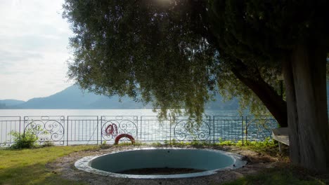 static shot of empty pool and tree facing lake como, italy (lago di como, italia) with sun sparkling on water at sunset