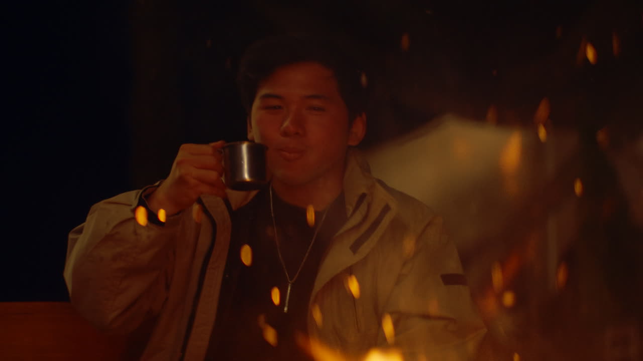 Man enjoying a drink by a campfire at night