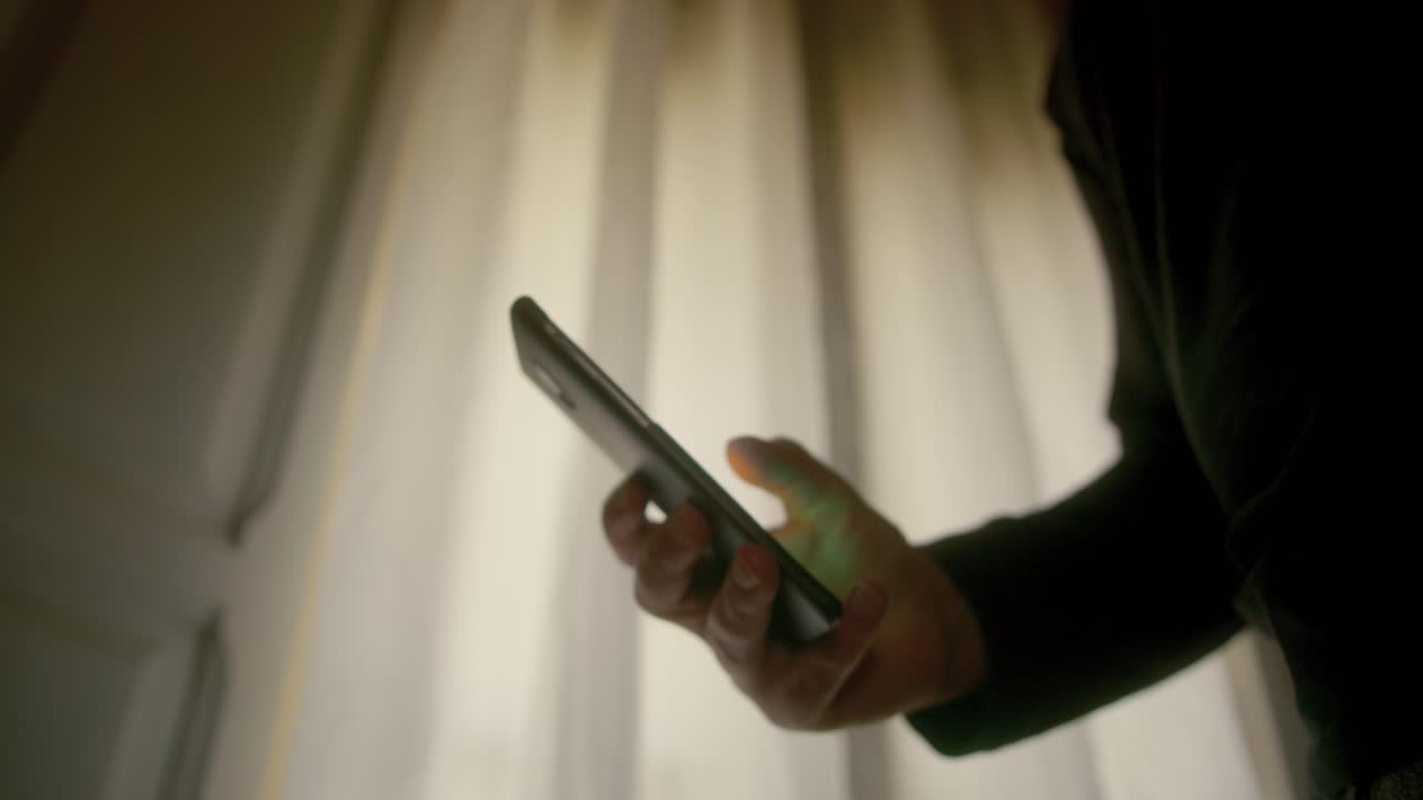 Uomo irriconoscibile che usa un cellulare 5G con il pollice vicino a una finestra di giorno, piano medio
