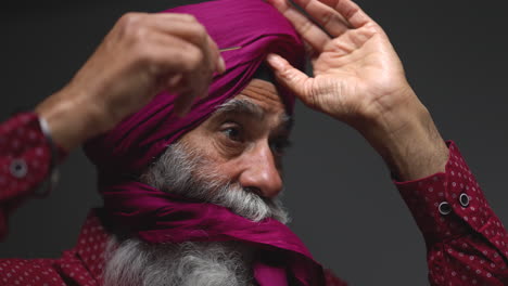 Primer-Plano,-Toma-De-Estudio-Con-Iluminación-Tenue-De-Un-Hombre-Sikh-Mayor-Con-Barba-Atando-Una-Tela-Para-Un-Turbante-Contra-Un-Fondo-Oscuro,-Filmado-En-Tiempo-Real