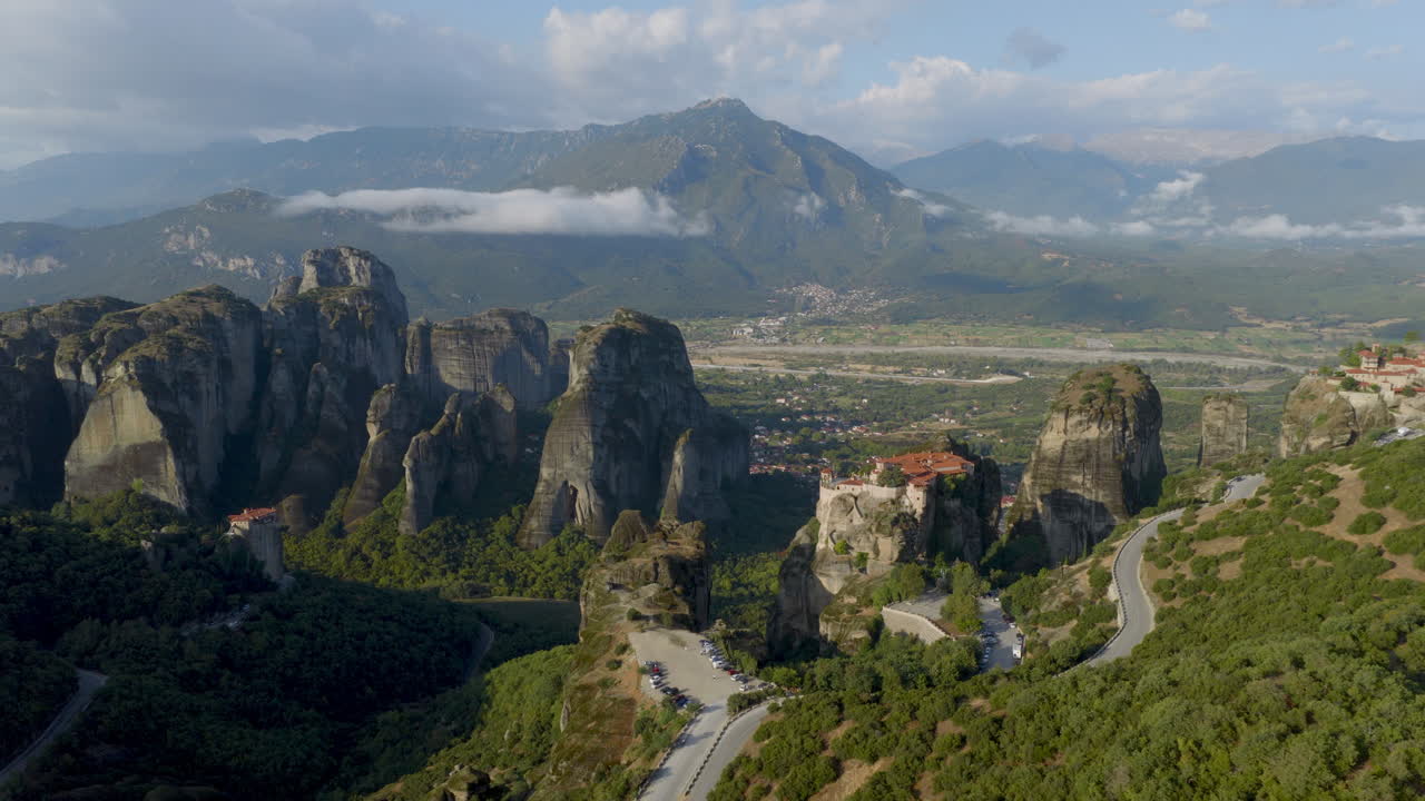 Cinematic aerial view of Meteora monastery in Greece perched on towering cliffs, dramatic rock formations and lush green valley create a breathtaking historic scene