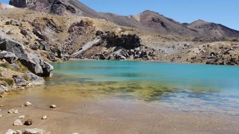 Tilt-pan-along-volcanic-lake-to-woman-tourist-hiking-Ngauruhoe-trail