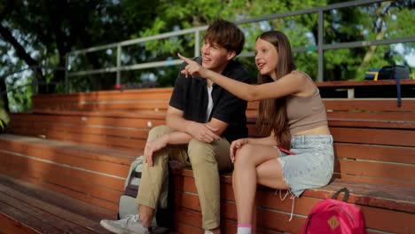 two teenagers sitting on a bench in a park, talking and laughing