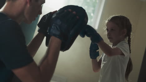 trainer with pads and punching child in gym. skilled instructor conducts sparring with little girl in boxing school slow motion. healthy hobby