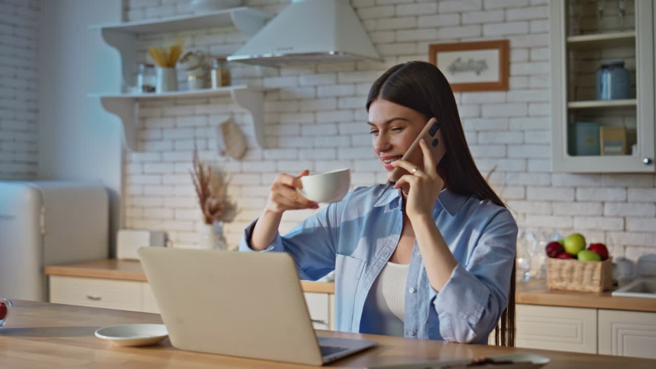 Freelancer tager et opkald på sin mobil i køkkenet (nærbillede). Pigen drikker kaffe.