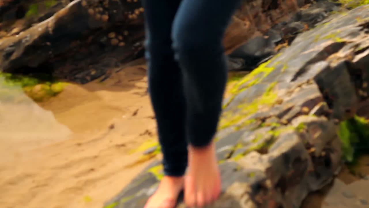 hermosa morena caminando a lo largo de las rocas por la playa