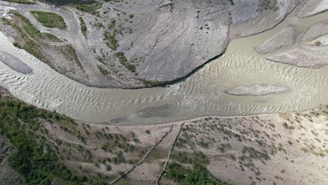 antena de arriba hacia abajo de un río marrón fangoso rodeado de arena negra que fluye río abajo en un día soleado