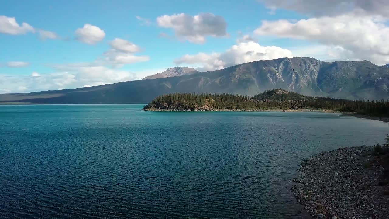 vuelo costero en verano sobre el agua de la costa del lago kluane azul turquesa de yukon hacia la isla jacquot y la impresionante cordillera en un día de cielo soleado, canadá, aproximación aérea aérea