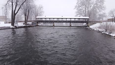 iconic roofed bridge during heavy snowfall, aerial fly toward view