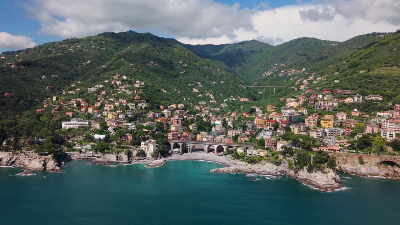 Ripresa aerea di una colorata città costiera italiana incastonata tra le montagne e il Mediterraneo.