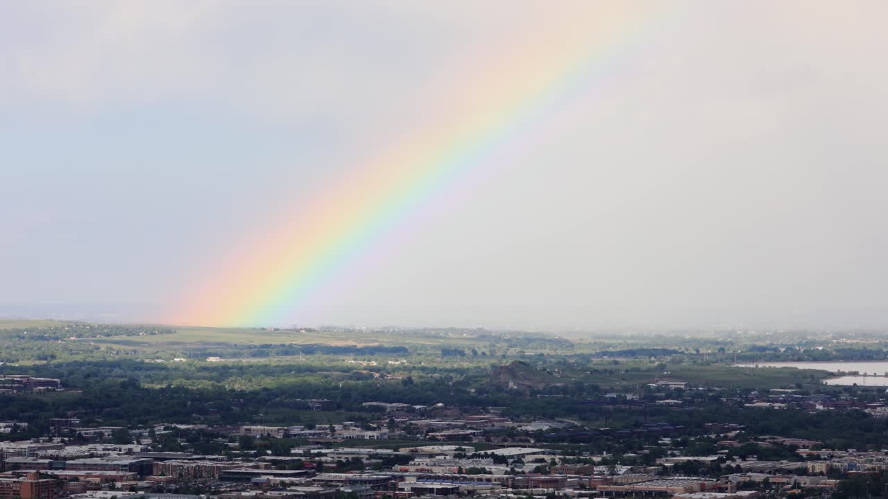 A rainbow bridges the sky over Boulder, Colorado, offering a moment of calm after a passing storm. Its reflection glimmers off rooftops and hillsides.