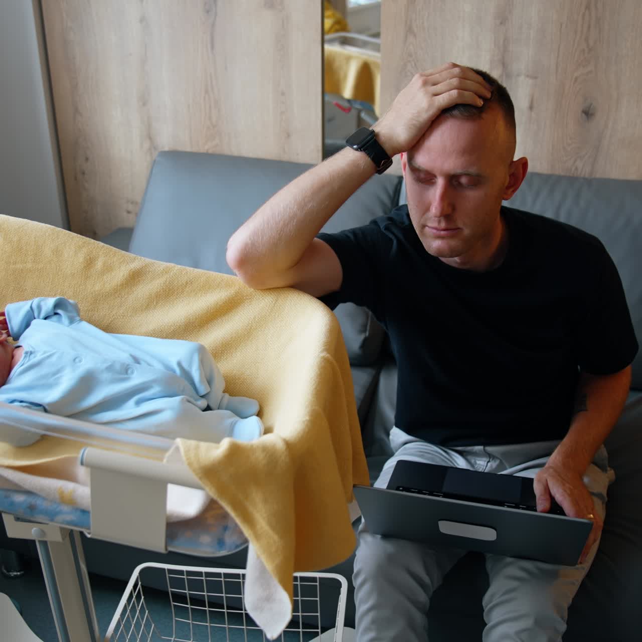 Busy modern dad working on laptop and watching a baby. Tired father falls asleep leaning on hand