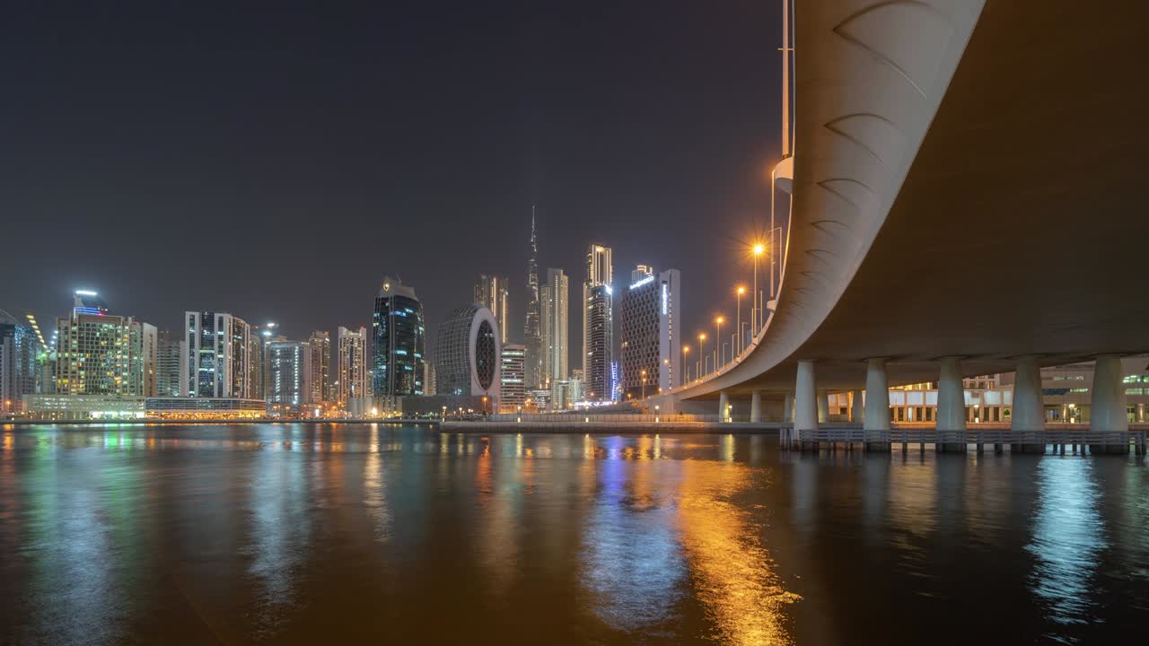 Time lapse with lake or river and bridge in Dubai Downtown skyline, United Arab Emirates or UAE. Financial district in urban city. Skyscraper buildings at night. Reflection.