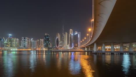 time lapse with lake or river and bridge in dubai downtown skyline, united arab emirates or uae. financial district in urban city. skyscraper buildings at night. reflection.