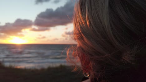 woman with windswept blond hair looking at sunset, close up, slow motion