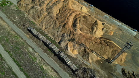 Aerial-of-sand-pile-building-construction-site-next-to-port,-drone-video