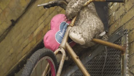 osito de peluche sucio dejado solo en una bicicleta montada creativamente en la pared con una almohada de corazón rosa diciendo mamá recuerdos emocionales de la infancia abandonados solos crecido sin un niño interior a cámara lenta