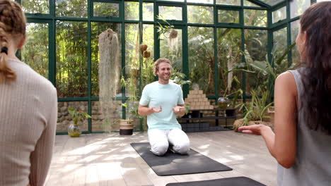 practicing yoga, man kneeling on mat in glass house with group