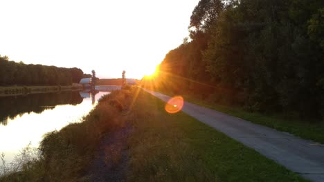 drone floats over a path and river with a dam and the sun setting on the horizon