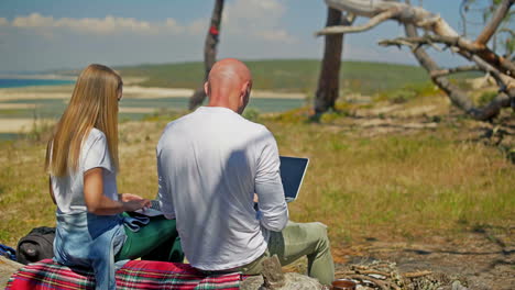 vista posterior de una pareja usando computadoras portátiles al aire libre