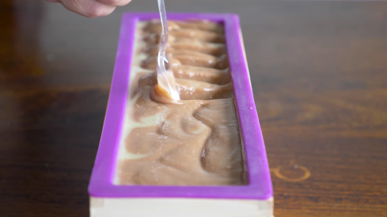 한 여성이 새로 만든 비누 블록을 숟가락으로 부드럽게 움직여 주형 전체에 예술가 패턴을 만들고 있습니다.