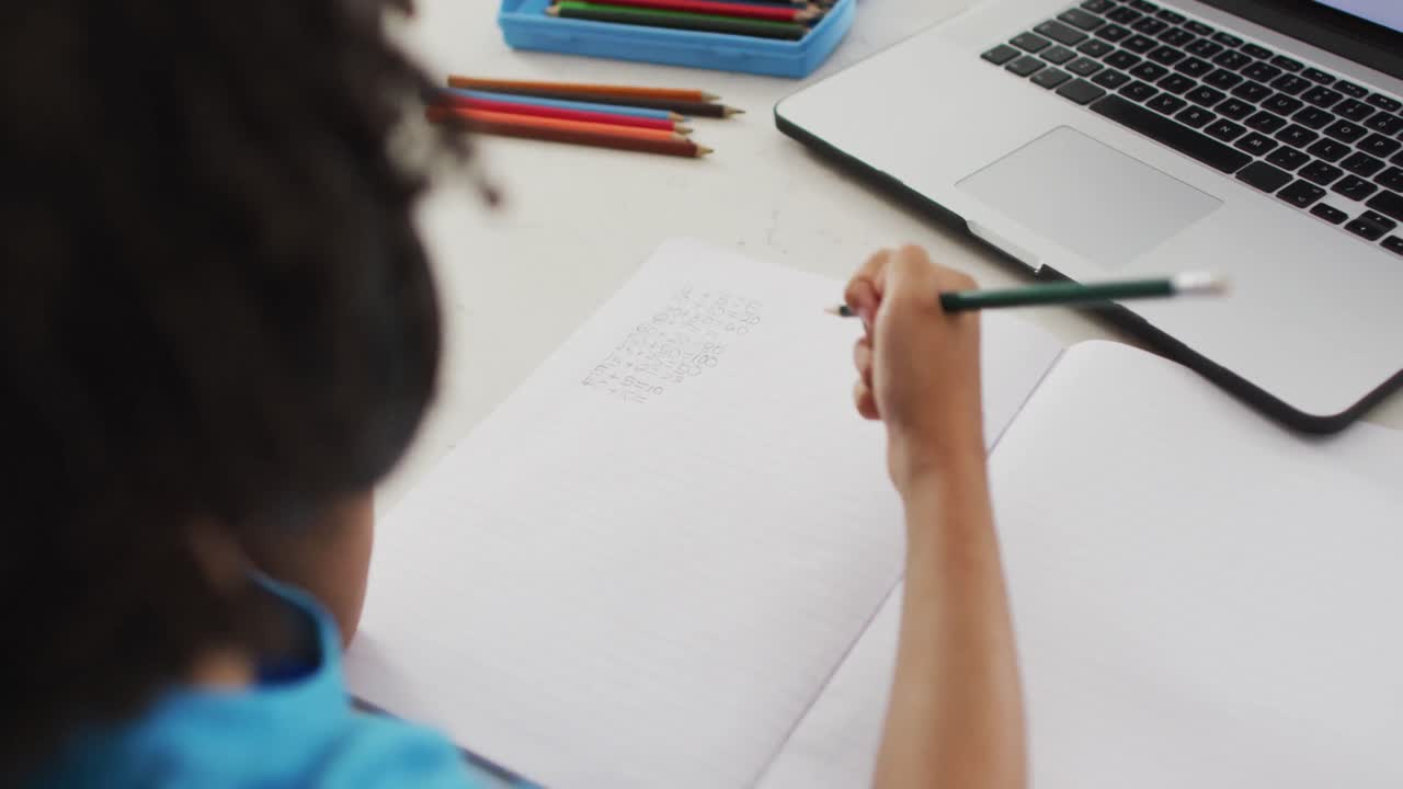 feliz muchacho biracial sentado en la mesa usando computadora portátil y teniendo clases en línea