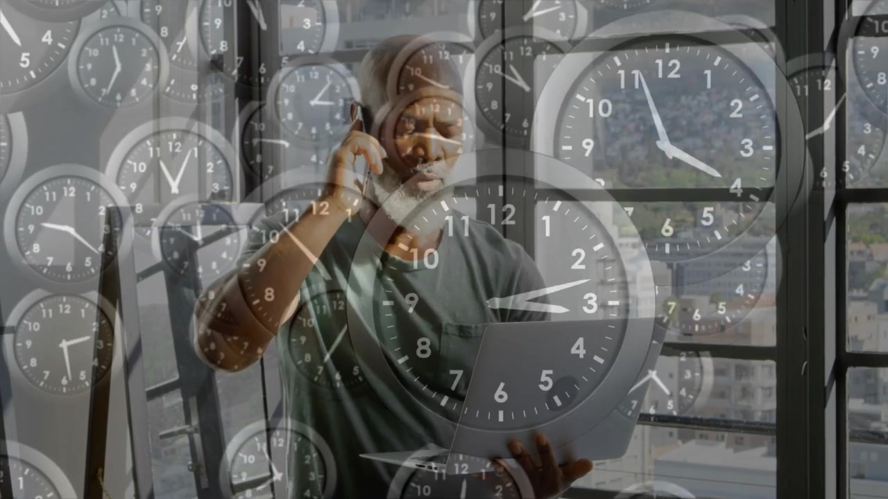 Mature man taking phone call while reading laptop, clocks overlay showing deadlines in business