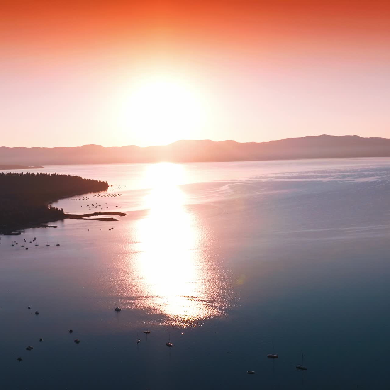 Amazing pink sunset over the lake. Sun reflecting on the smooth surface of water. Multiple boats on water
