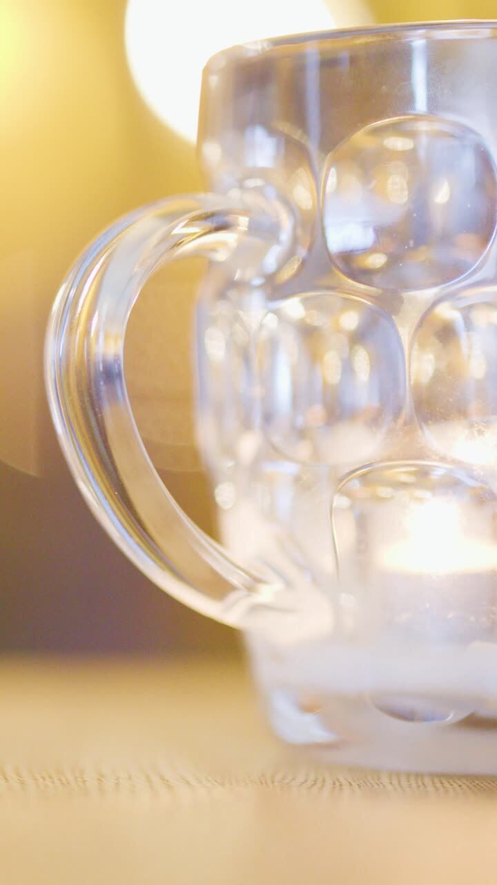 A clear glass mug sits on a table with a softly glowing candle behind it, warm ambient lighting, and a shallow depth of field