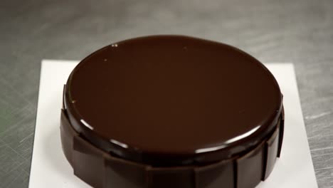 Hand-smoothing-glossy-chocolate-glaze-on-cake-for-a-perfect-finish,-in-a-professional-kitchen