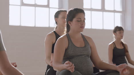 young pregnant hispanic woman in yoga class practicing lotus pose enjoying group meditation practice relaxing in fitness studio at sunrise