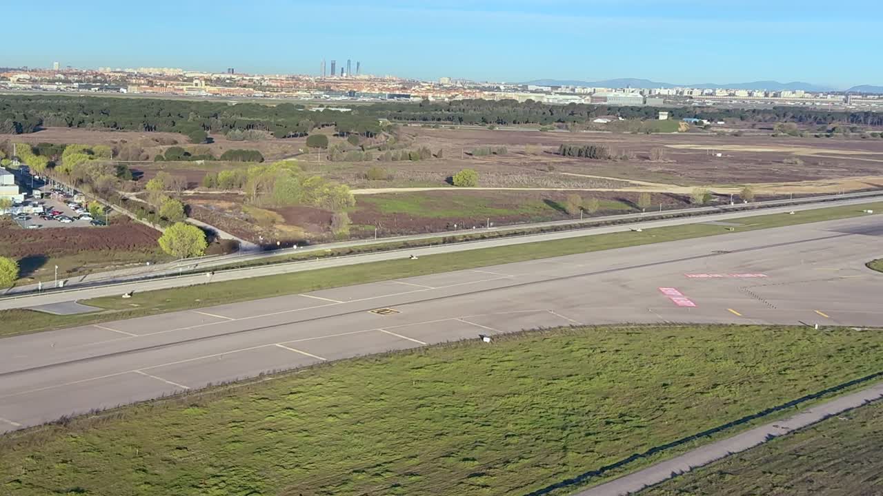 Uma vista da janela esquerda do cockpit da sombra de um avião a jato em aproximação final ao aeroporto de Madrid, com a cidade de Madrid ao fundo sob um céu azul.