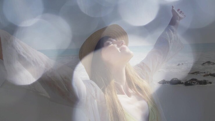 Donna in posa con le braccia aperte sulla battigia, un'overlay bokeh che si ritira e rivela abbigliamento da spiaggia per il viaggio.