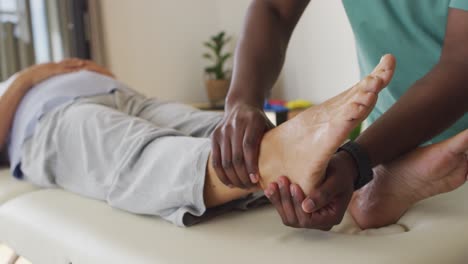 video of hands of african american male physiotherapist exercising with caucasian senior woman