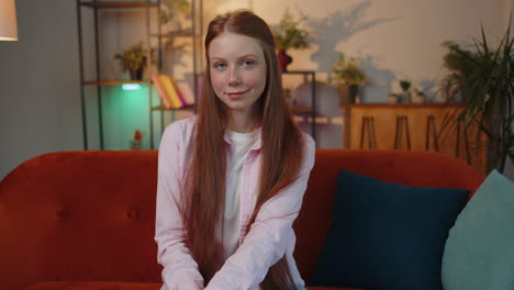 Close-up-of-happy-beautiful-young-redhead-child-girl-smiling-looking-at-camera-at-home-on-couch